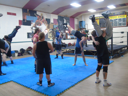A coach is watching over the trainees as they lift their partners in the air for a body slam