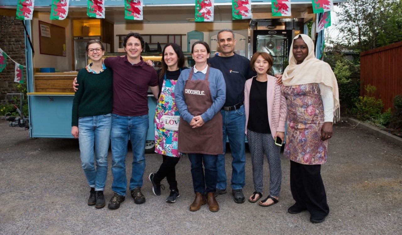 The team members of Oasis refugee centre in Cardiff stand outside a kitchen decorated with Welsh flags