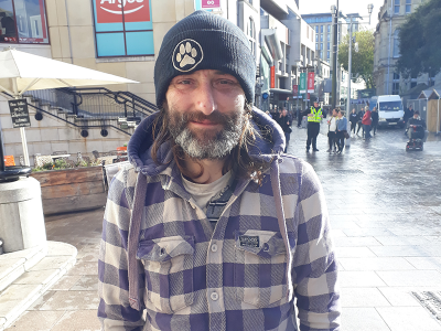 A man who looks scruffy standing in the middle of a busy street