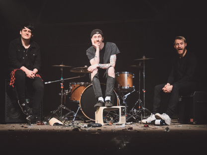 Three men are sat on a stage