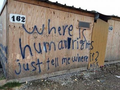 A shelter in a Calais refugee camp showing the words: where is humanity just tell me where?