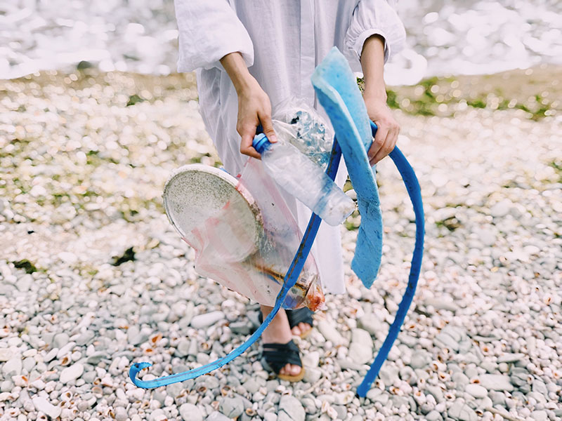girl walking on sand holding plastic waste