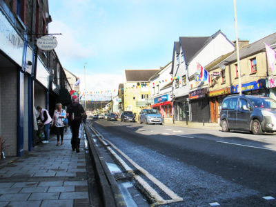 Treorchy high Street on a Saturday, showing shoppers and shop fronts, and flags and bunting
