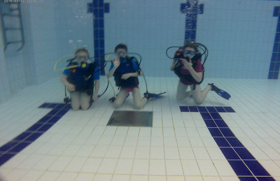 three people diving in deep end of swimming pool