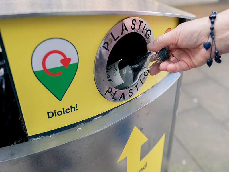 Someone putting a plastic bottle in a yellow recycling bin