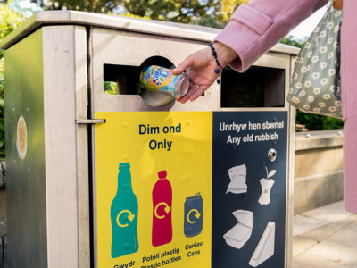 someone putting a plastic bottle in a yellow recycling bin