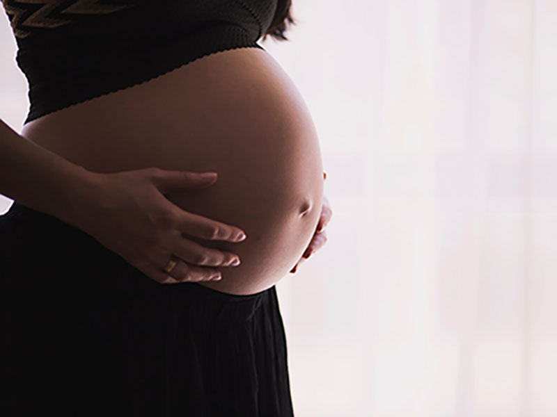 A photo of a pregnant woman holding her stomach alone in a room to represent The Birth Partner Project's initiative to support isolated pregnant women.