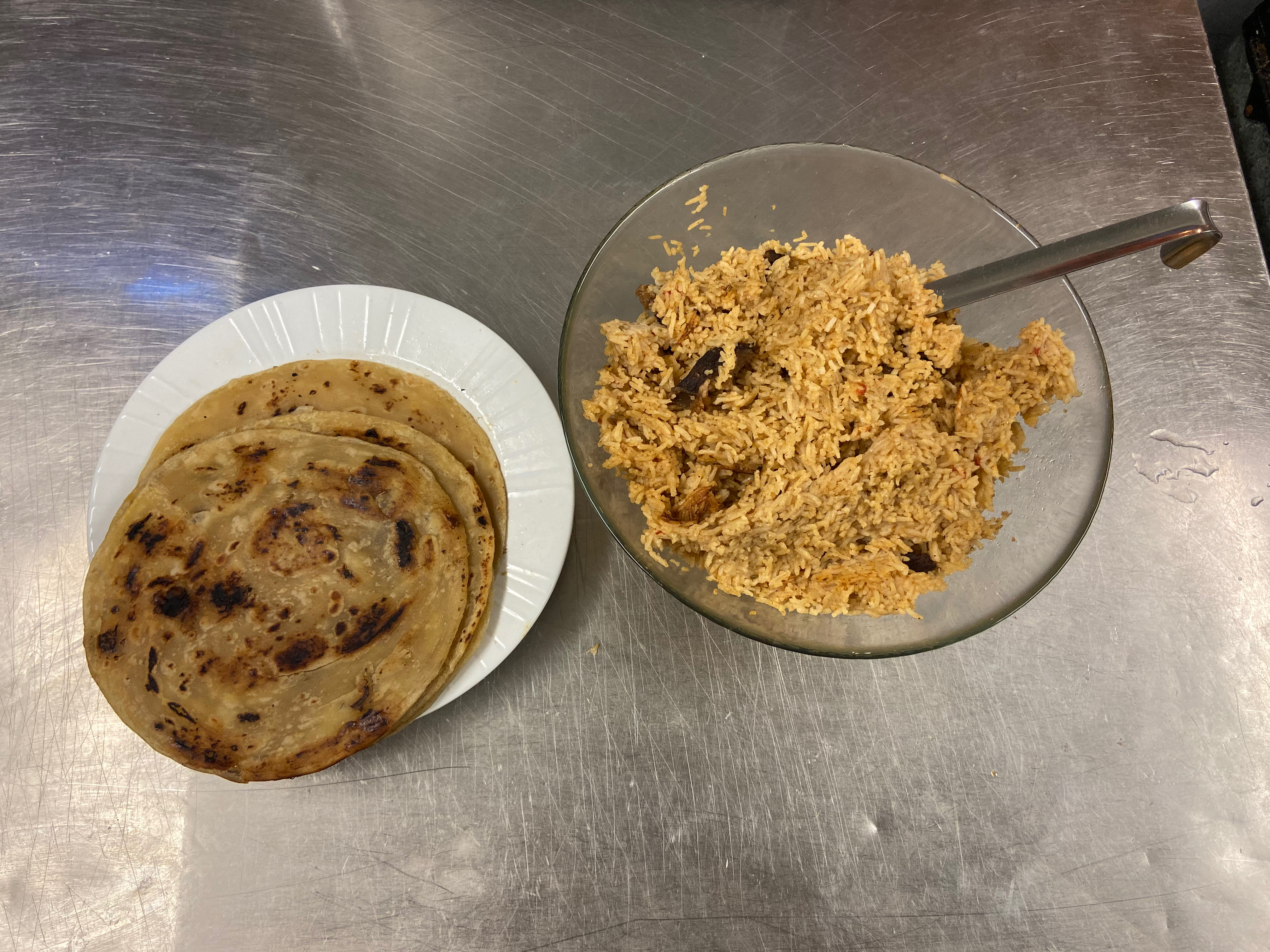 A plate of flatbreads and a rice and goat curry sit on a kitchen surface