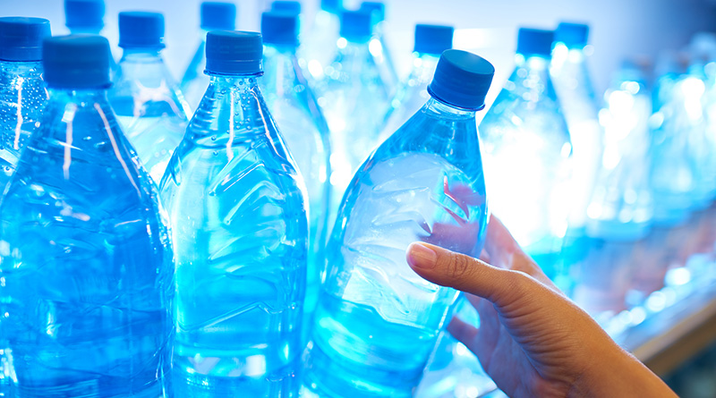 Human hand taking mineral water from shelf in supermarket