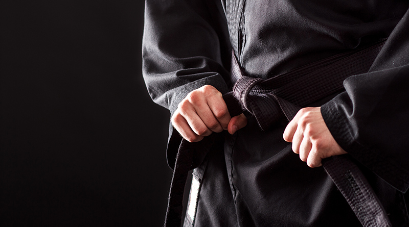 Closeup of male karate fighter tying the knot to his black belt