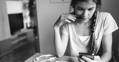 Young woman with braided hair sitting by the table, looking on her smart phone. Paying bills on the phone.